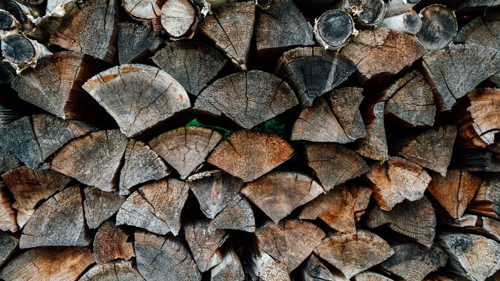 Pile de bûches fendues au bois grisé, rangées face coupée vers l'avant
